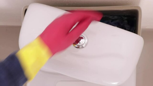 Close up de manos con guantes rojos poniendo pastilla azul desinfectante en WC