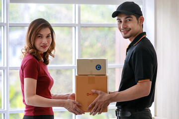 Smiling Asian courier man delivers packages to Asian female customer at home. Parcel delivery and shipping, door to door e-commerce business concept.