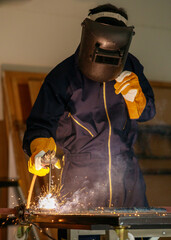 Image of a welded steel plate welding in an industrial factory. He wears complete protective equipment such as masks, gloves, welding suits. This kind of work requires specific skills.