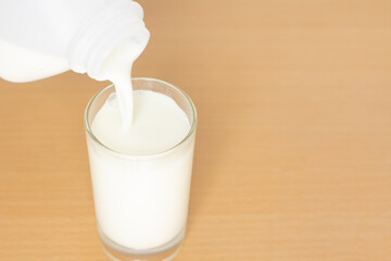 Pouring pure milk drink in bottles plastic in glass is naturally healthy food placed on a wood deck in the background with copy space for text.