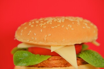 Hamburger.chicken burger  on a bright red background.Hamburger day holiday.Fast food. Delicious fresh burger with chicken cutlet and fresh vegetables.Fast food and snacks
