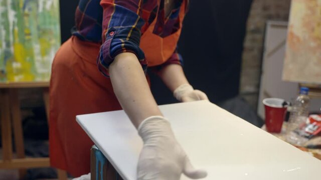 Women artists smering white glue on the canvas. Artistic collaboration in workshop.