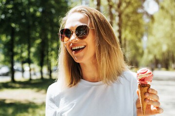 Attractive laughing young woman with glasses eating ice cream, outdoors. Portrait of a beautiful,...