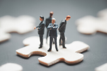 Four miniature businessman standing back to back and standing on jigsaw puzzle piece