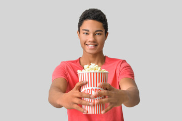 African-American teenager with popcorn on light background