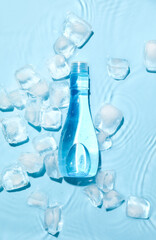 Bottle of cosmetic product and ice cubes in water on color background