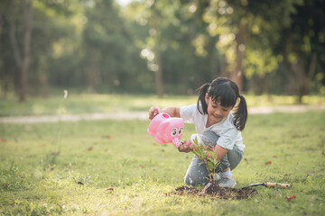 Asian little child girl pouring water on the trees. kid helps to care for the plants with a watering can in the garden.