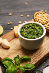 Board with bowl of fresh pesto sauce and ingredients on dark wooden table