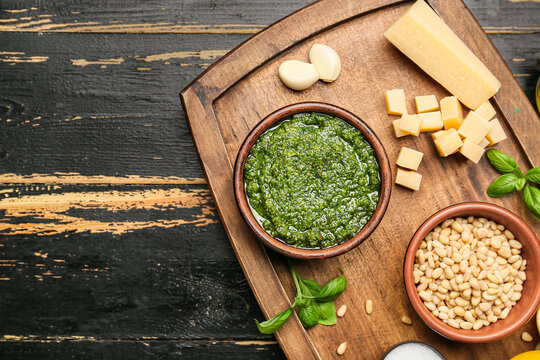 Board with fresh pesto sauce and ingredients on dark wooden table