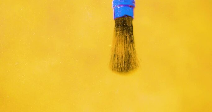 Cleaning a paint brush in water. 4K Close up of a thick paintbrush dipping into and rinsing in golden glittery water and swirling round.