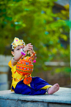 happy Janmashtami Greeting Card showing Little Indian boy posing as Shri krishna or kanha/kanhaiya with Dahi Handi picture and colourful flowers.