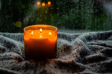Burning aroma candle puts on table with cloth near by window that have rain drop in monsoon season....