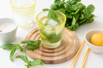 Glass of lemonade with basil on light background