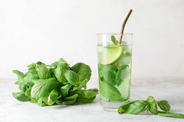 Glass of lemonade with basil on light background