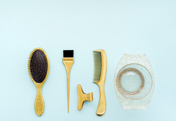 Hairdressing tools in gold color on a blue background. Hair salon accessories for coloring, bowl, comb, brush, top view.