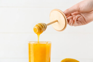 Woman pouring honey from dipper into glass on light background