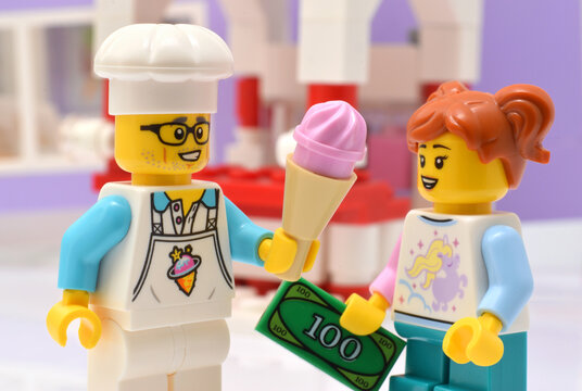 Lego minifigure ice cream salesman and young girl is paying money. Editorial illustrative image of hot summer.