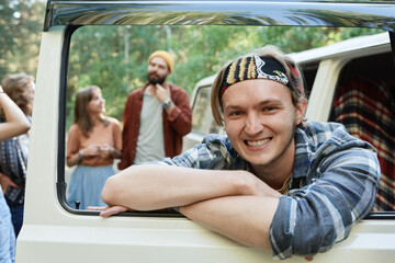 Fototapeta na wymiar Portrait of guy smiling at camera sitting in the van with his friends in the background