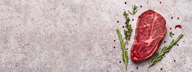 Fresh marbled beef rib eye steak and spices on grey stone banner, copy space