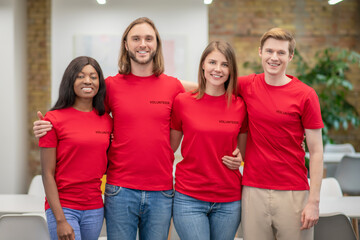 Group of smiling young people volunteers standing embracing