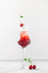 Cherry liqueur with ice and berries on a gray background. A refreshing summer alcoholic drink