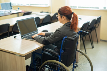 Young woman works at a laptop while sitting in a wheelchair in a university lecture hall....