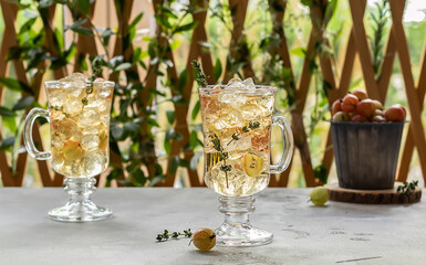 Two glasses with homemade gooseberry ice tea or lemonade with thymes. Summer cold drink with ripe berries and ice. 