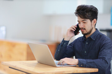 Young asian man talking on phone and working on laptop.