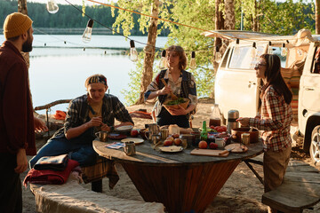 Group of friends setting the table and having lunch during their picnic in the forest