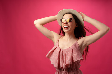 Studio fashion portrait of a young attractive woman in hat and glasses against pink backgorund