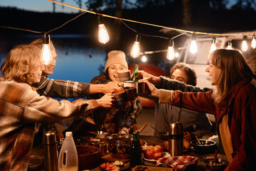 Group of young friends toasting with drinks and having fun during picnic on the nature