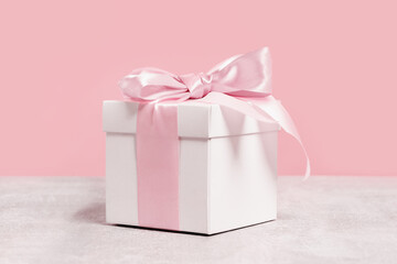 White gift box with shining pink ribbon bow on pink background. Gift or holiday concept. Mothers...
