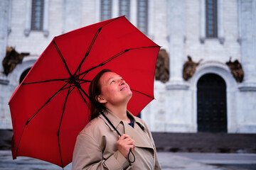 Happy woman with a red umbrella at an Orthodox church