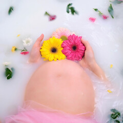 Pregnant woman holds gerbera flowers near her stomach in a tub of water