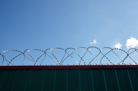 Metal wall with barbed wire against the blue sky background. Fence with barbwire for protection, space for text