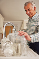 Mature Man At Home In Kitchen Washing Used Packaging  Before Recycling