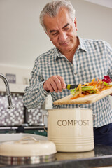 Mature Man In Kitchen Making Compost Scraping Vegetable Leftovers Into Bin