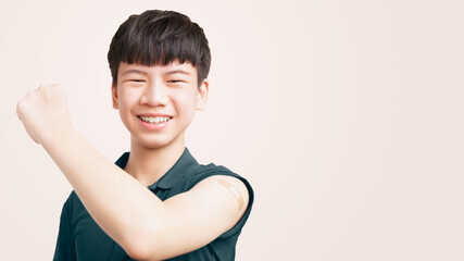 COVID 19 Vaccines for teenagers concept. Studio portrait of a healthy Asian teen boy lift his arm up to show the band aid from first dose vaccine shot. Against coronavirus, Back to school, Smile