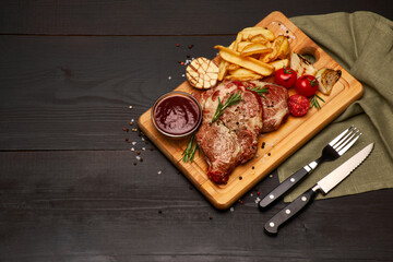 Grilled roated beef steaks, potato and sauce on wooden cutting board