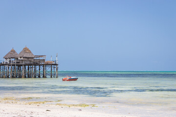 Wooden pier with boat and beach hut on sunny day. Low tide of Indian Ocean. Idyllic exotic resort. Pier in perspective with bungalows. Tropical paradise. Honeymoon in lagoon. Scenic tranquil seascape.