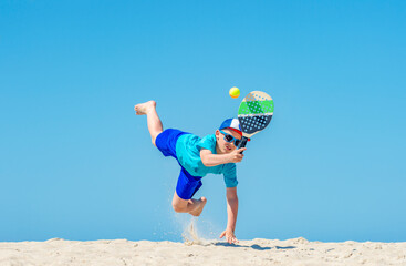 Young boy playing tennis on beach. Summer sport concept.