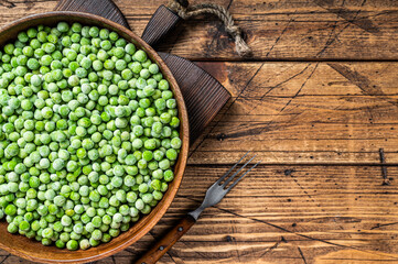 Obraz na płótnie Canvas Cold Frozen green peas in a wooden plate. Wooden background. Top view. Copy space