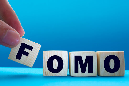 FOMO, acronym for Fear of Missing Out in wooden alphabet letters isolated on blue background