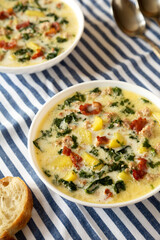 Homemade Zuppa Toscana with Kale and Bread in a white bowl, low angle view.
