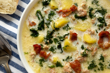 Homemade Zuppa Toscana with Kale and Bread in a white bowl, top view. Flat lay, overhead, from above. Close-up.