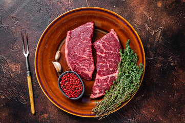 Fresh Raw denver or top blade meat steak on a rustic plate with thyme. Dark background. Top view