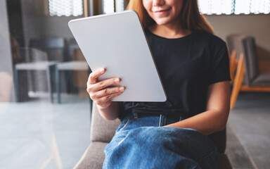 Closeup image of a beautiful young asian woman holding and using digital tablet in cafe