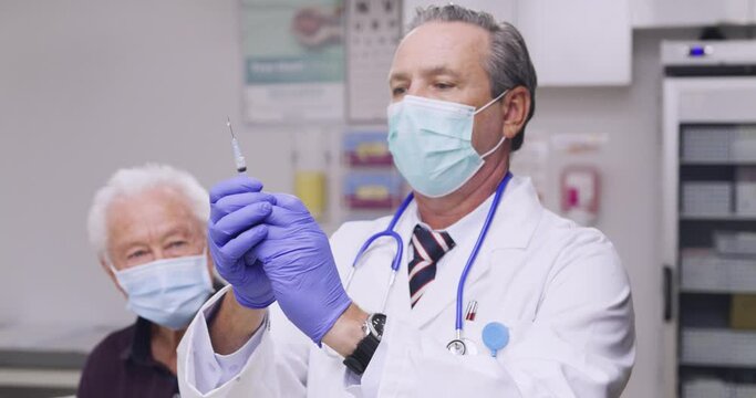 A Mid Shot Of An Australian Male Medical Doctor Administering A Covid-19, SARS-CoV-2 Vaccine Injection With A Needle and Syringe, To An Elderly Man. Wearing Safety Gloves And Protective Mask