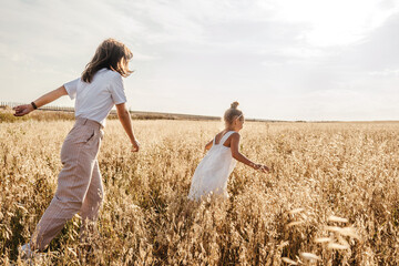 Young mother and daughter run in field.