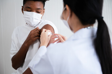 Obraz premium Female doctor or nurse vaccinating against coronavirus 19 at the shoulders African-American man. By wearing a mask at all times. Concept of preventing the spread of COVID-19.
